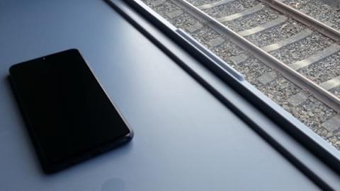 Ein Mobiltelefon liegt am Fenster eines Zuges. Im Hintergrund sind Schienen zu sehen.