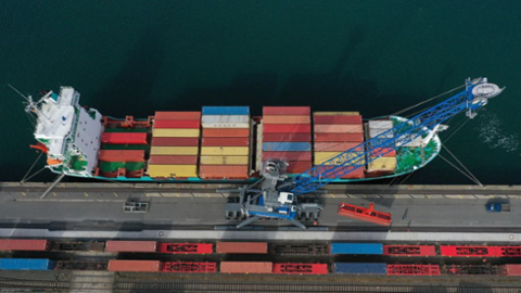 Luftaufnahme eines Container-Schiffes neben einer Gleisanlage