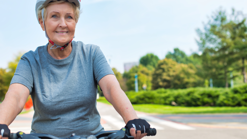 Eine ältere Dame mit Fahrradhelm fährt lächelnd auf einem Fahrrad